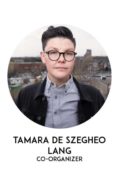 Image of Tamara De Szegho Lang. Person wearing a ligth blue shirt and a dark cardigan, with short dark hair and glasses. Photo is taken on a roof