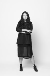 a person standing against a white background wearing a black dress and black shoes with their arms crosses