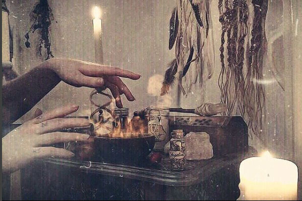 a grainy image of hands above an alter with a candle and feathers and other magical objects
